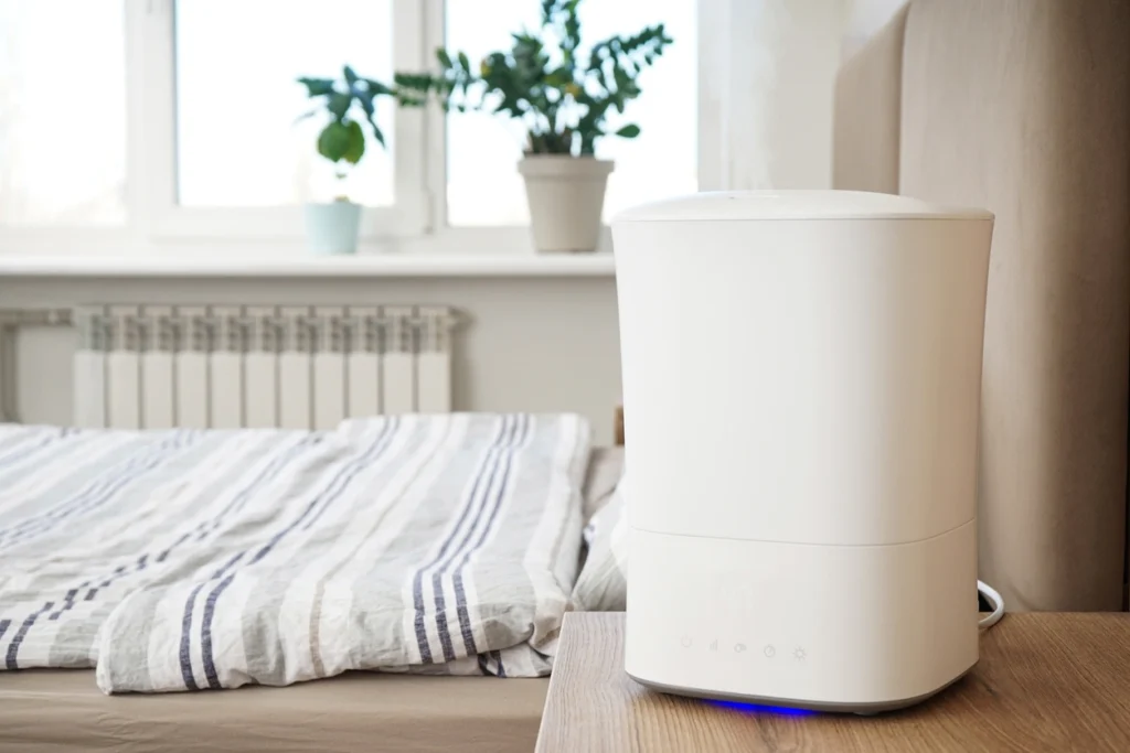 A white air purifier placed on a neatly made bed, showcasing its sleek design and functionality in a bedroom setting.