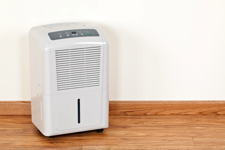A white air conditioner placed on a wooden floor, showcasing its sleek design and functionality in a room setting.
